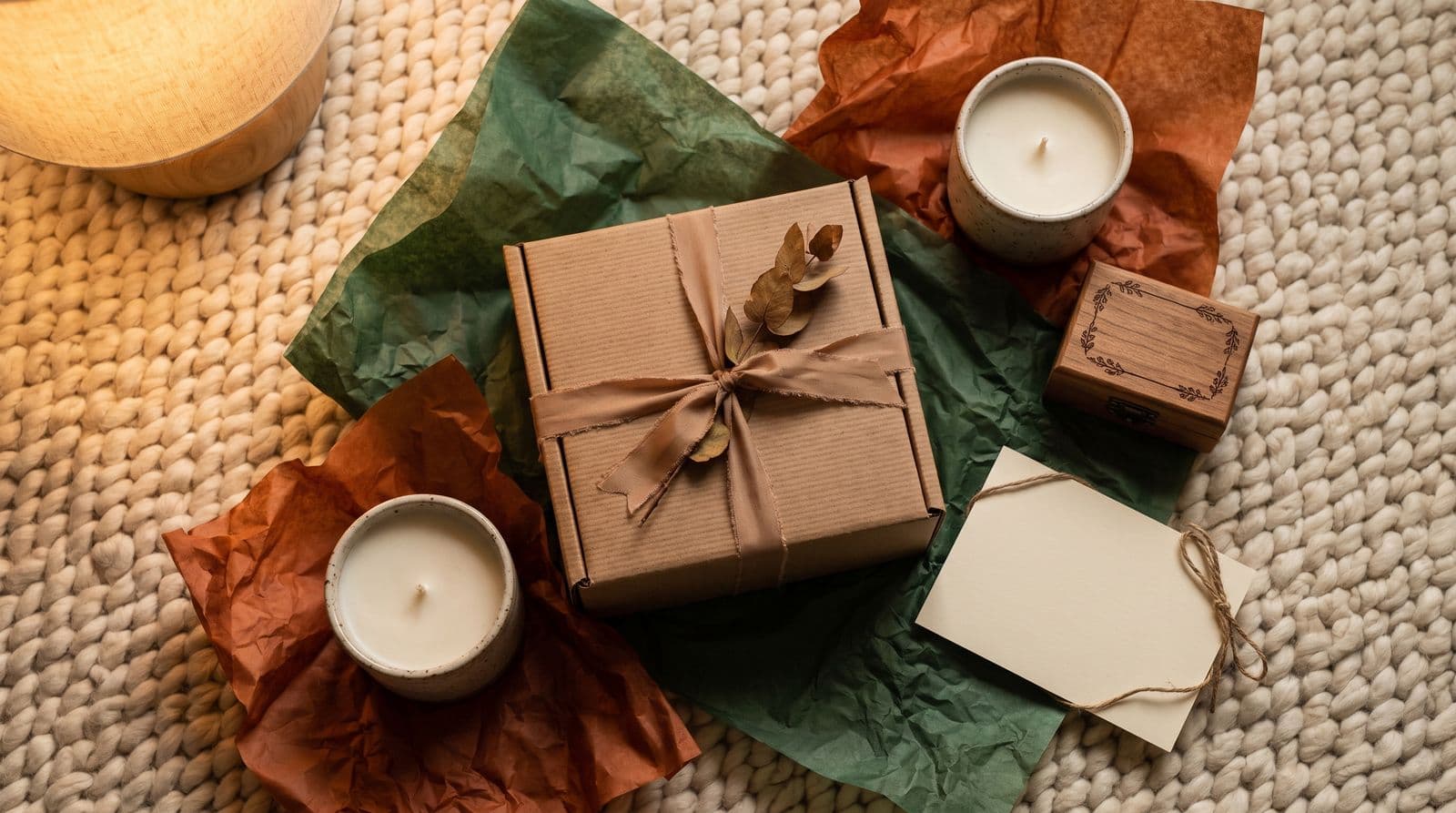 A beautifully wrapped housewarming gift sits on a cozy rug, surrounded by a candle and a small wooden keepsake box as a welcome gesture for a relocated employee.