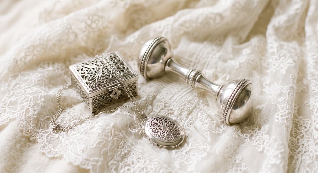 Silver filigree keepsake box, engravable oval locket on a fine chain and a traditional silver baby rattle on ivory lace